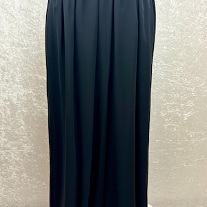 Puede incluir: Una falda larga negra con cintura alta y tejido fluido. La falda se muestra en un maniqu&iacute;, destacando su dise&ntilde;o plisado y su elegante ca&iacute;da. El color oscuro y el dise&ntilde;o sencillo sugieren versatilidad.