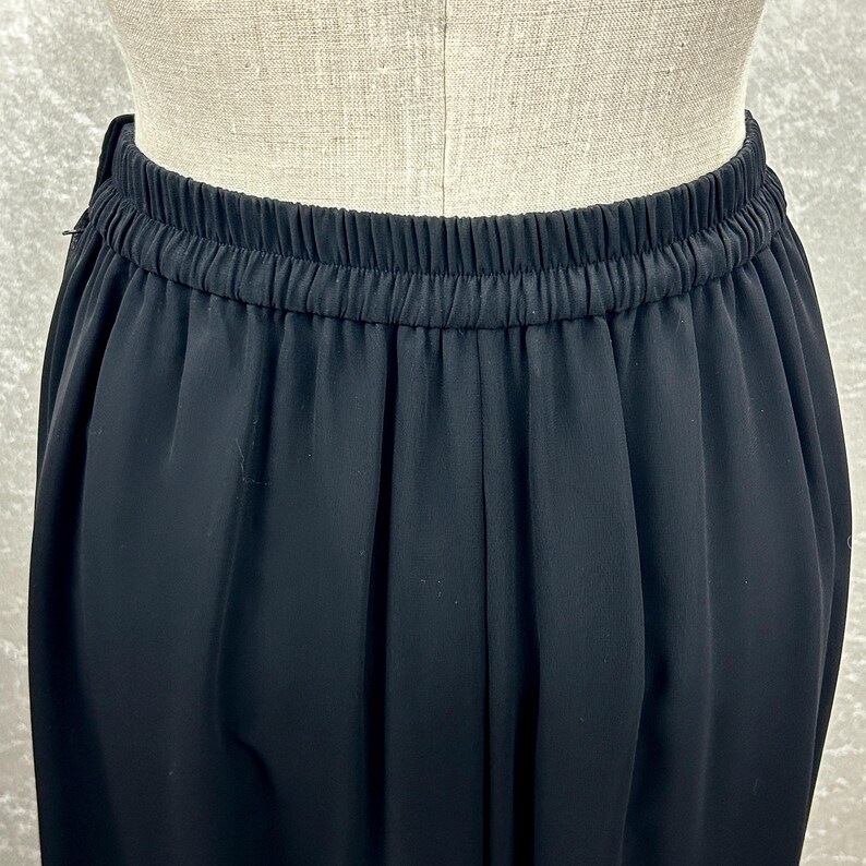 Puede incluir: Primer plano de un pantal&oacute;n negro con cintura el&aacute;stica. La tela es suave y cae desde la cintura. El pantal&oacute;n se muestra en un maniqu&iacute;.