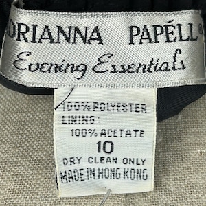Puede incluir: Primer plano de una etiqueta de prenda. La etiqueta dice "ORIANNA PAPELL Evening Essentials". La etiqueta tambi&eacute;n indica que la prenda es 100% poli&eacute;ster con forro 100% acetato. La talla es 10 y solo limpieza en seco. Hecho en Hong Kong.