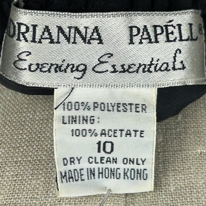 Puede incluir: Primer plano de una etiqueta de prenda. La etiqueta dice "ORIANNA PAPELL Evening Essentials". La etiqueta tambi&eacute;n indica que la prenda es 100% poli&eacute;ster con forro 100% acetato. La talla es 10 y solo limpieza en seco. Hecho en Hong Kong.