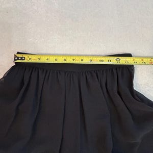 Puede incluir: Falda negra con cintura fruncida, medida con una cinta m&eacute;trica amarilla. La cintura de la falda mide aproximadamente 33 cm de ancho. La tela parece ser un material ligero y fluido.