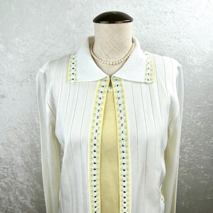 May include: A white cardigan with a yellow and green trim. The cardigan has a collared neckline and a button closure. The cardigan is on a white mannequin.