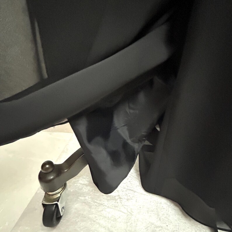 Puede incluir: Primer plano de una tela negra, posiblemente una falda o un vestido, con un forro oscuro. Una rueda de madera con rodamiento es visible en la parte inferior, lo que sugiere un mueble. La tela se extiende sobre la rueda.