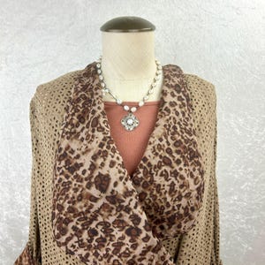 May include: A tan open-front jacket with a perforated design is layered over a rust-colored top. A scarf with a brown leopard print is draped over the shoulders. A pearl necklace with a silver pendant completes the look. Fashion apparel.