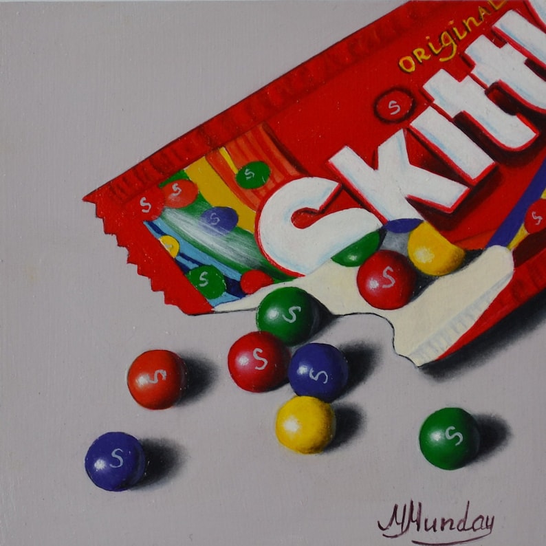 Op de afbeelding: Een rode en witte zak Skittles snoepjes met het woord "Skittles" erop gedrukt. De zak is open en er vallen een aantal Skittles snoepjes uit. De snoepjes zijn rood, oranje, geel, groen en paars.