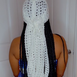 May include: White crochet hair scarf with a long, flowing design. The scarf is worn over black braids.