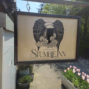 May include: Wooden sign for Stumbie Inn, featuring a black graphic of a beer glass with wings and grapes. The sign is framed in dark wood and hangs from chains. The text "Stumbie Inn" and "Scarborough" are visible.