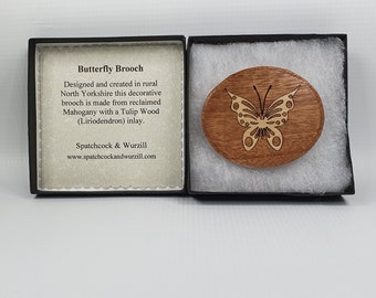 May include: A wooden butterfly brooch in a gift box. The brooch is made from reclaimed mahogany with a tulip wood inlay. The text on the box reads "Butterfly Brooch" and "Designed and created in rural North Yorkshire this decorative brooch is made from reclaimed Mahogany with a Tulip Wood (Liriodendron) inlay. Spatchcock & Wurzill www.spatchcockandwurzill.com"