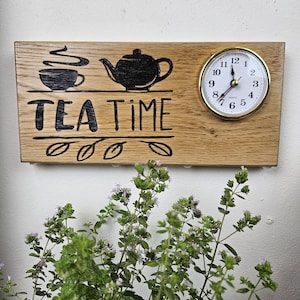 May include: Wooden wall clock with a tea theme. The clock features a black illustration of a teacup and teapot, with the words "TEA TIME" below. A round clock with a gold-colored bezel is on the right side.