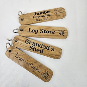 May include: Four wooden key fobs with silver key rings. The key fobs have text that reads "Jumbo Personalised Key Fob", "Log Store", "Grandad's Shed", and "Lorna's Room". The key fobs are made of light brown wood.