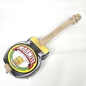 Könnte beinhalten: Eine originelle Gitarre in Form eines Marmite-Glases. Der Korpus zeigt das ikonische Marmite-Logo in Rot, Gelb und Grün. Hals und Griffbrett sind aus hellem Holz gefertigt, und sie hat sechs Saiten.