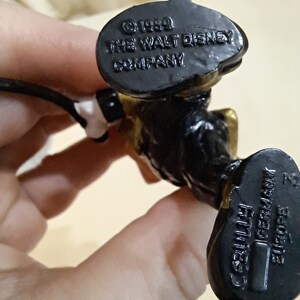 May include: Black and gold plastic figurine of Mickey Mouse wearing a conductor's uniform. The bottom of the figurine has the text "&copy; 1990 THE WALT DISNEY COMPANY" and "GERMANIA" with a barcode.
