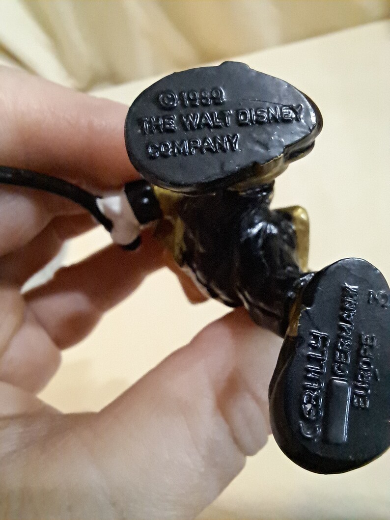 May include: Black and gold plastic figurine of Mickey Mouse wearing a conductor's uniform. The bottom of the figurine has the text "&copy; 1990 THE WALT DISNEY COMPANY" and "GERMANIA" with a barcode.