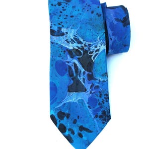 Peut inclure: Une cravate bleue avec un motif marbré. La cravate présente des nuances de bleu et de noir, créant un design abstrait unique. La cravate est faite d'un tissu lisse et convient aux occasions formelles ou semi-formelles.