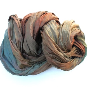 May include: A draped silk scarf in shades of brown, teal, and rust. The fabric is bunched and folded, creating a textured appearance. The scarf is likely hand-dyed, with colour variations throughout.