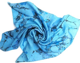 May include: A light blue silk scarf with a marbled pattern in shades of blue and gray. The scarf is artfully draped, showcasing the intricate design and soft texture. This accessory adds a touch of elegance.