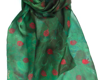 May include: A rectangular scarf in a deep forest green hue featuring a marbled pattern and a repeating print of small red roses. The fabric has a translucent, lightweight quality. The word Silkraft is printed in white near the bottom left corner.