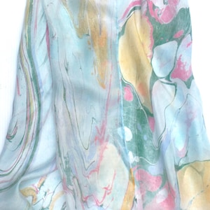 May include: A lightweight fabric scarf featuring a marbled pattern with swirling colours of light blue, soft pink, pale yellow, and muted green. The design displays fluid, organic shapes and overlapping hues that create a soft, blended appearance.