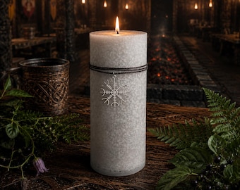 May include: A tall, cylindrical, textured grey pillar candle with a lit wick. A dark brown cord is wrapped around the upper portion of the candle, featuring a silver-toned metal charm shaped like a Vegvisir compass symbol hanging from the cord.