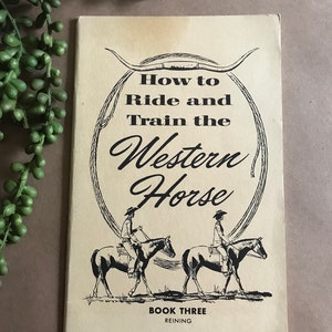 以下が含まれることがあります： 「How to Ride and Train the Western Horse」というタイトルのヴィンテージブックで、馬に乗った2人のライダーの白黒イラストが描かれています。この本は「Book Three: Reining」とラベル付けされています。