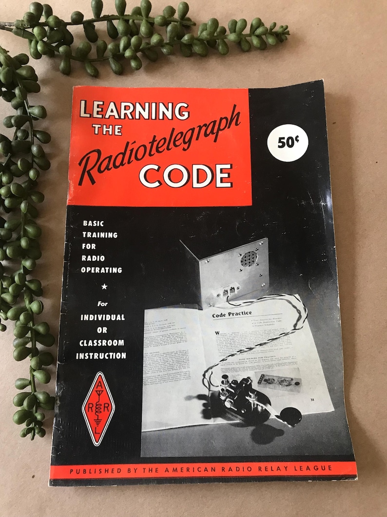 May include: Vintage book titled "Learning the Radiotelegraph Code" with a red and black cover. The book includes text about radio operating and classroom instruction. A price of 50&cent; is visible on the cover.