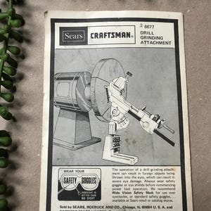 Peut inclure: Publicité en noir et blanc pour un accessoire de meulage de perceuse Sears Craftsman. L'image présente un schéma de l'outil, avec le texte « Wear Your Safety Goggles ». La publicité est marquée « Made in U.S.A. ».
