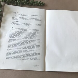 May include: Open book with text on the left page and a blank right page. The text is in black font and includes words like "SENTIRE", "KHANATE", and "TANTAMOUNT". A green plant is in the upper left corner.