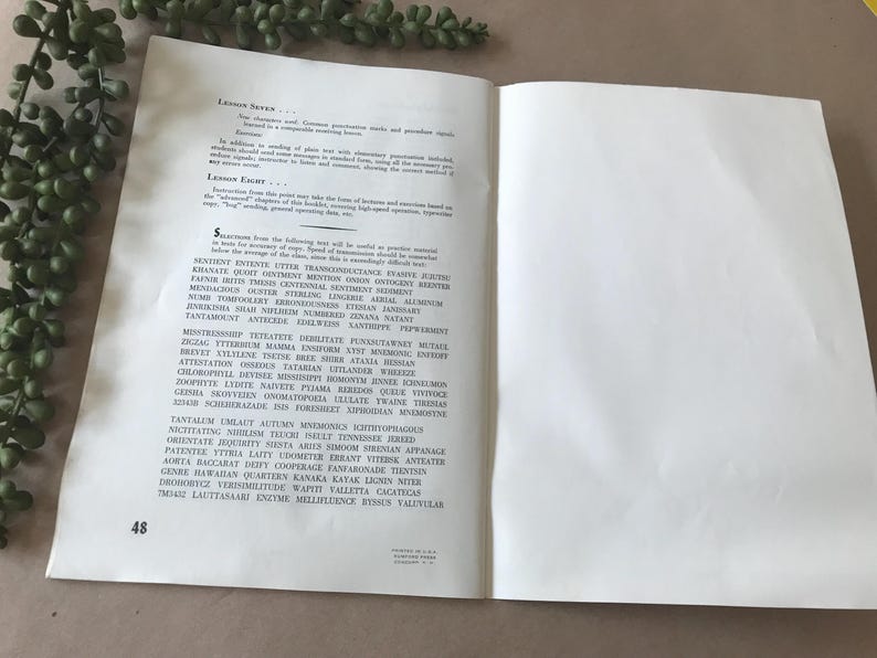 May include: Open book with text on the left page and a blank right page. The text is in black font and includes words like "SENTIRE", "KHANATE", and "TANTAMOUNT". A green plant is in the upper left corner.