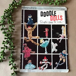 May include: A vintage book cover with the title "Doodle Dolls: Simple-Easy to make!"  The cover features a grid of 10 different yarn doll designs, including a clown, a ballerina, a monkey, and a graduation cap.