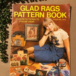May include: A book titled "Glad Rags Pattern Book" featuring a woman sitting on the floor. The book cover showcases a range of leather craft projects, such as bags, purses, and belts. The text on the cover reads "Over 50 patterns to choose from" and "Stock No. 1914".