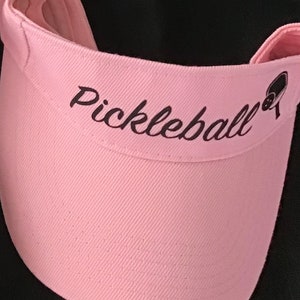 May include: Pink visor with black embroidery that reads "Pickleball" and a small pickleball icon.