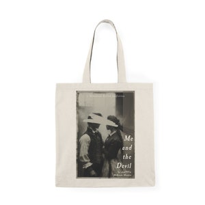 May include: A beige tote bag with a black and white image of a couple on the front. The image is from a vintage photograph and the text "Me and the Devil" is printed below the image. The text "a Sebastian Sellow fiction" is printed above the image.
