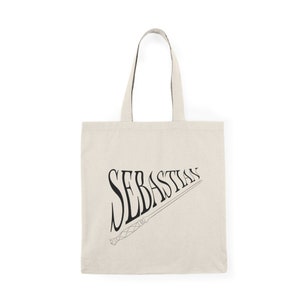 May include: A beige canvas tote bag with black text that reads "Sebastian" and a black and white illustration of a wand.