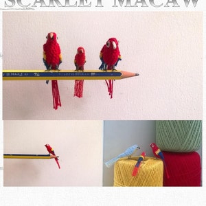 Puede incluir: Patrón de amigurumi para una guacamaya escarlata, un tipo de loro. El patrón es de Vinamigurumi. La imagen muestra tres guacamayas de crochet posadas en un lápiz, y dos guacamayas más en ovillos de lana.
