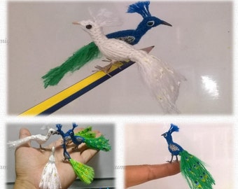 May include: Amigurumi pattern for a peacock, with instructions by Vinamigurumi. The pattern includes images of a white peacock with green tail feathers, a blue peacock with green tail feathers, and a blue peacock with green and yellow tail feathers.