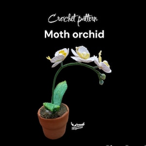 Może przedstawiać: Wzór na szydełku na białą orchideę motylkową z żółtymi środkami. Orchidea znajduje się w doniczce z terakoty z zielonymi liśćmi. Wzór nazywa się "Moth Orchid" i pochodzi od "Needle Tinygurumi".