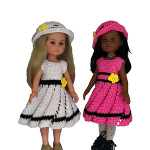 May include: Two dolls wearing crocheted dresses and hats. The doll on the left is wearing a white dress with black trim and a white hat with a yellow flower. The doll on the right is wearing a pink dress with black trim and a pink hat with a yellow flower.