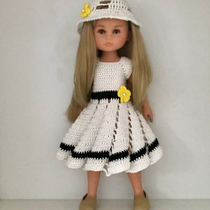 May include: A white crocheted dress with black stripes and yellow flower accents. The doll is wearing a white crocheted hat with yellow flowers and brown shoes.