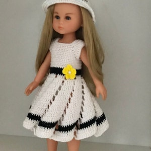 May include: A white crocheted dress with black trim and a yellow flower accent. The doll is wearing a white crocheted hat and brown shoes.