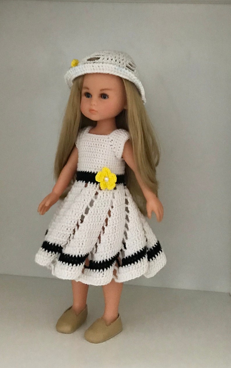 May include: A white crocheted dress with black trim and a yellow flower accent. The doll is wearing a white crocheted hat and brown shoes.