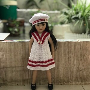 May include: A white crocheted dress with red stripes and a white crocheted sailor hat with a red stripe. The doll is wearing black shoes.