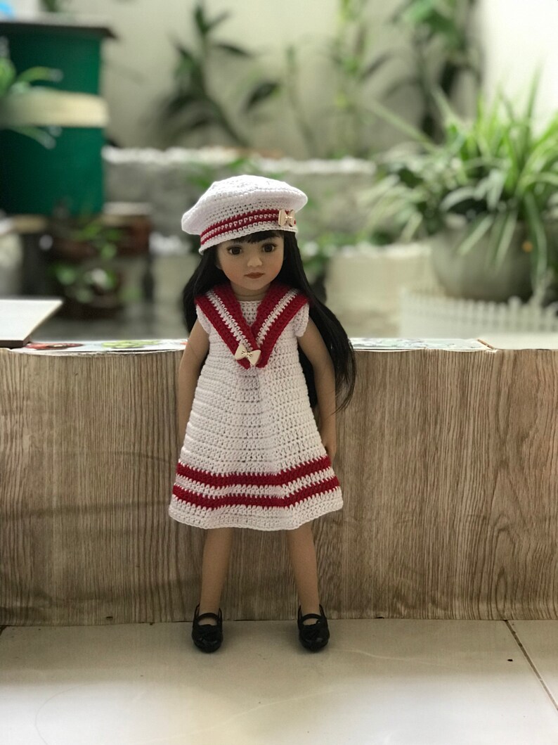 May include: A white crocheted dress with red stripes and a white crocheted sailor hat with a red stripe. The doll is wearing black shoes.