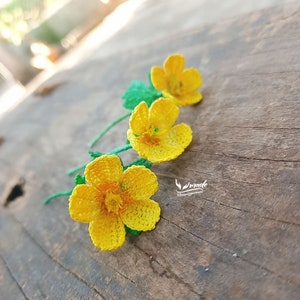 May include: Three crocheted yellow flowers with green stems on a wooden surface.