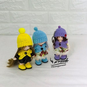 Puede incluir: Tres muñecas de crochet con sombreros y atuendos de diferentes colores. Las muñecas llevan sombreros amarillos, azules y morados y tienen el pelo largo y castaño. Las muñecas están de pie sobre una superficie blanca. El texto "made Vinamigurumi" es visible en la esquina inferior derecha de la imagen.