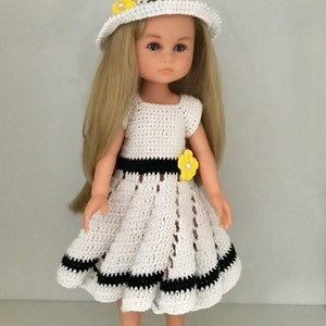 May include: A white crocheted dress with black trim and yellow flower accents. The dress is worn by a doll with blonde hair and a white crocheted hat with a yellow flower.