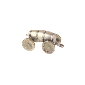 May include: A silver charm in the shape of a barrel on wheels. The barrel has a textured surface and the wheels are round with a slightly raised center.