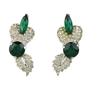 May include: A pair of vintage earrings featuring a leaf design. Each earring has a large, round, emerald-green gemstone, a smaller marquise-cut green stone, and is encrusted with clear, sparkling rhinestones. The earrings have a silver-tone metal setting.