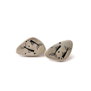 May include: A pair of silver earrings with a unique design featuring black stylized figures on a silver background.