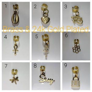 May include: Nine gold-plated ear cuffs with different charms, including a seashell, heart, eye, ankh, honeycomb, dragonfly, the word "Sexy", and a padlock. The ear cuffs are labeled with numbers 1 through 9. The text "Brass & 24k Gold Plated" is displayed below the first row of ear cuffs.