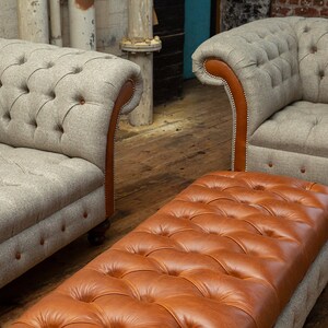 May include: A brown leather tufted ottoman with a gray tweed sofa in the background.